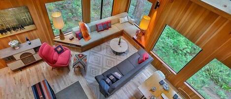 A spacious room with a large window, a sofa, a dining table, and a red chair.