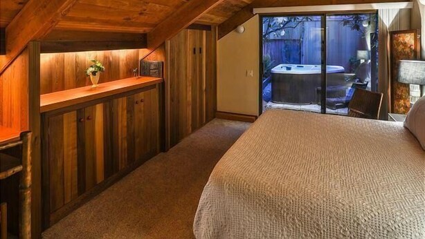 Een slaapkamer met een groot bed, houten plafond en een schuifdeur naar een buitensauna.
