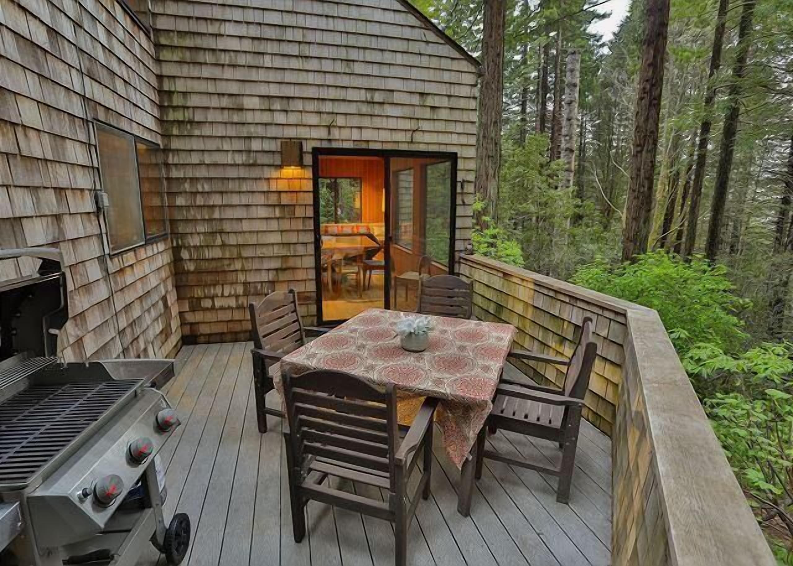 A wooden deck with a table and chairs, a grill, and a glass door leading to an interior space.