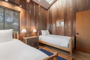A bedroom with two beds, wooden walls, a skylight, and a window with blinds. - Gray Whale | Hot Tub Nights & Meadow Views (The Sea Ranch)