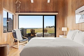 A bedroom with a large bed, a view of the ocean, and a seating area with chairs.
