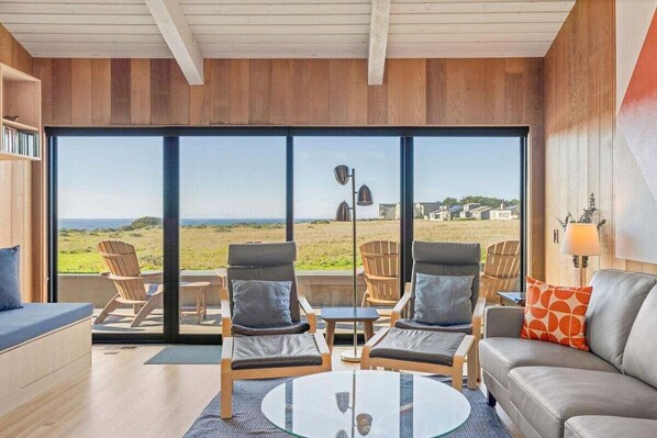 A modern interior with a large window, a sofa, two armchairs, and a small table.