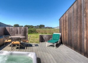 Eine Holzterrasse mit Whirlpool, einem Tisch mit Stühlen und einer Liege.