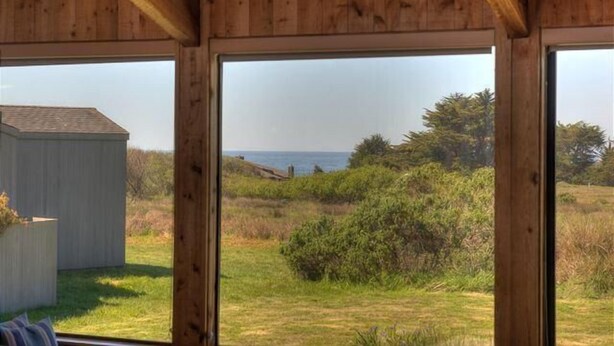 Un intérieur en bois avec de grandes fenêtres donnant sur un paysage verdoyant et un plan d’eau.