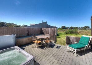 Eine Holzterrasse mit Whirlpool, einem Tisch mit Stühlen und einer Liege.