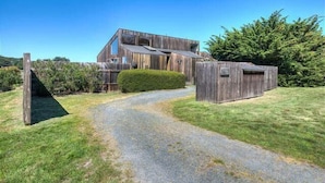 Une maison moderne en bois, avec une allée en gravier menant à un portail en bois.