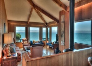 Uma sala de estar ampla com pé direito alto, grandes janelas e vista para o mar.
