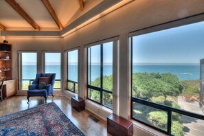 A room with large windows, a blue armchair, a patterned rug, and a wooden floor.