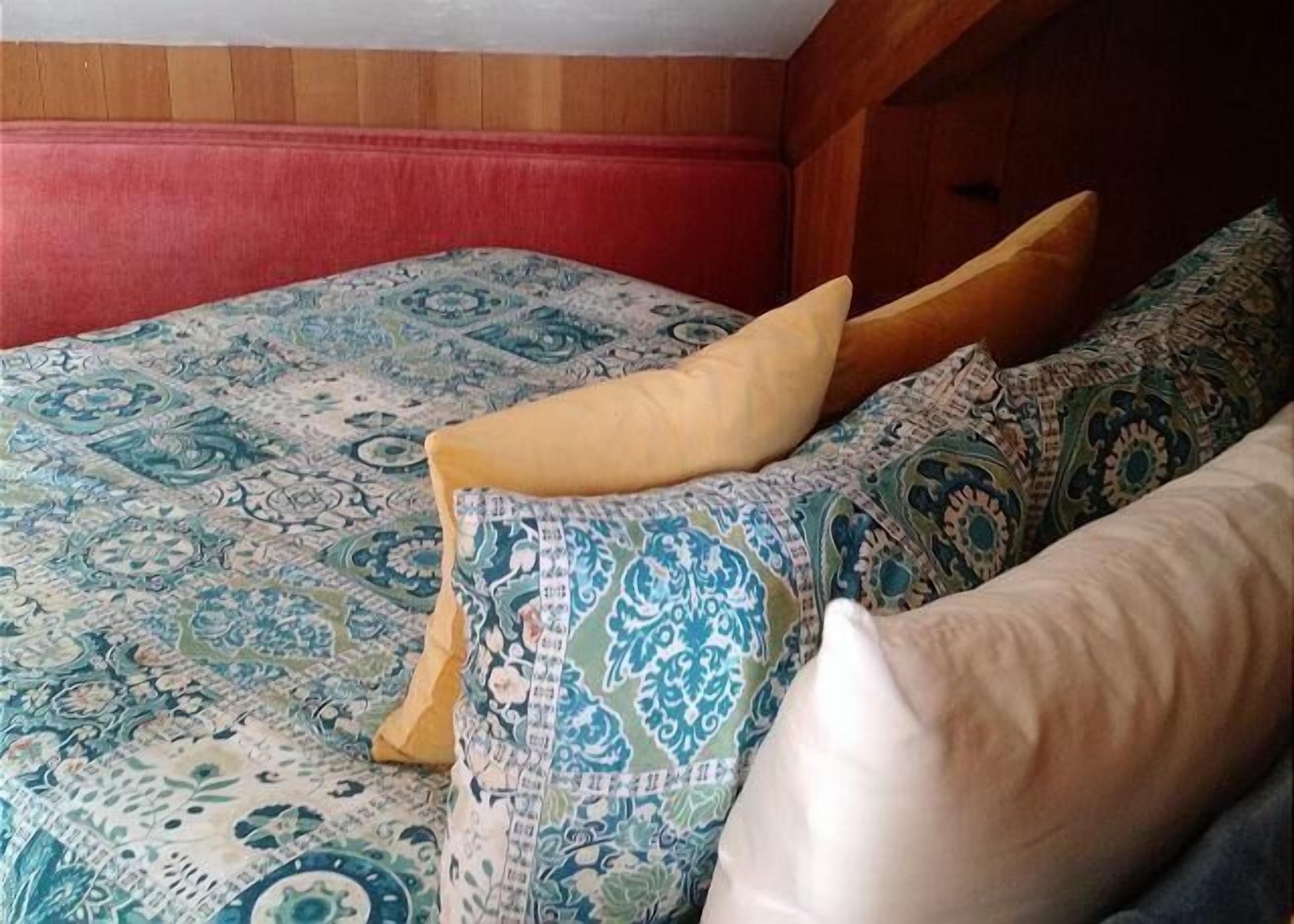 A bed with patterned bedding and pillows, a wooden headboard, and a red wall.