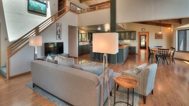 A spacious living area with a sofa, armchairs, and a coffee table. A staircase leads to an upper level.