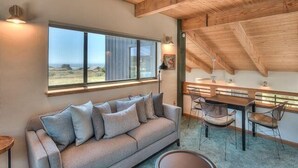 A modern interior with a sofa, dining table, chairs, and a large window offering a view.