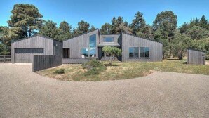 A modern two-story building with a flat roof, large windows, and a gravel driveway.