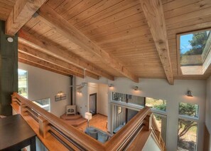 A wooden interior with a staircase, a dining area, and a view through large windows. - Sandpiper Nest | Coastal Escape Near Walk On Beach (The Sea Ranch)
