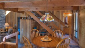 A wooden interior with a round dining table, chairs, and a stained glass light fixture.