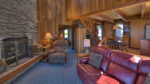 A spacious living area with a stone fireplace, leather sofa, and wooden beams.