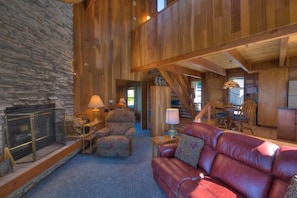 A spacious living area with a stone fireplace, leather sofa, and wooden beams. - Second Wind | Coastal Bliss & Hot Tub (The Sea Ranch)