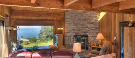 A cozy interior with a stone fireplace, wooden beams, and a view of the outdoors.