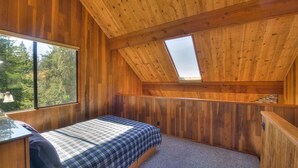 A bedroom with a sloped ceiling, a bed, a desk, and a large window.