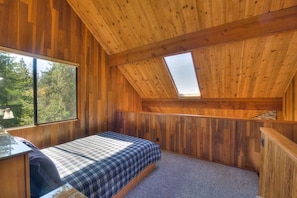 A bedroom with a sloped ceiling, a bed, a desk, and a large window. - Second Wind | Coastal Bliss & Hot Tub (The Sea Ranch)