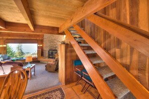 A wooden interior with a staircase, a stone fireplace, and a view through a window. - Second Wind | Coastal Bliss & Hot Tub (The Sea Ranch)