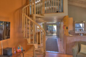 A spacious living area with a wooden spiral staircase, a television, and a kitchen area with a wooden counter.