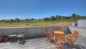 An outdoor deck with a wooden table and chairs, surrounded by a concrete wall, overlooking a grassy field. - Silver Mist | Pool with Stargazing Decks (The Sea Ranch)