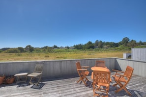 An outdoor deck with a wooden table and chairs, surrounded by a concrete wall, overlooking a grassy field.