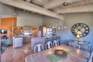 A spacious kitchen with wooden beams, a dining area with a clock, and a staircase leading to an upper level.