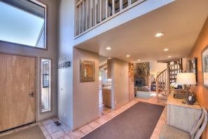 A spacious interior with a high ceiling, a fireplace, and a staircase leading to an upper level.