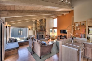 A spacious living area with a stone fireplace, seating arrangements, and a kitchen area.
