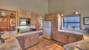 A kitchen with wooden cabinets, a microwave, a refrigerator, and a window with a view. - Silver Mist | Pool with Stargazing Decks (The Sea Ranch)