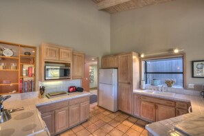 A kitchen with wooden cabinets, a microwave, a refrigerator, and a window with a view.