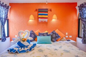 Una camera da letto con una parete arancione, un letto con molti cuscini, una coperta a righe blu e bianche e un asciugamano a forma di cuore.