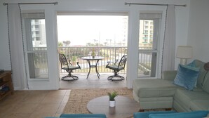 Una sala de estar con un sofá verde, dos sillones, una mesa de centro y un balcón con vistas a edificios y una calle.