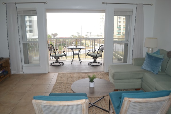 Uma sala de estar com um sofá verde, duas poltronas, uma mesa de centro e uma varanda com vista para edifícios e uma rua.