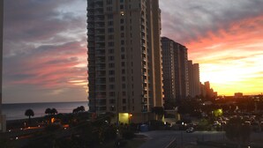 Un hotel moderno de gran altura con varios pisos, balcones y vistas al océano al atardecer.