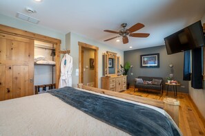 A bedroom with a large bed, wooden wardrobe, a vanity with a mirror, a ceiling fan, a TV mounted on the wall, and a small table with a plant. - Jumping Off Point · Your Jumping Of Point for Livingston Adventures! (Livingston)