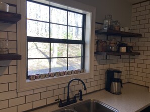 A kitchen with a window, a sink, and shelves with kitchen items.