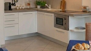 A compact kitchen with white cabinets, a microwave, a stove, and a sink. - "SEA HOUSE" DIRECTLY ON THE SEA (Pomonte)