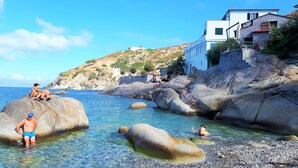 A coastal scene with clear water, large rocks, and a white building with a stone facade. - "SEA HOUSE" DIRECTLY ON THE SEA (Pomonte)