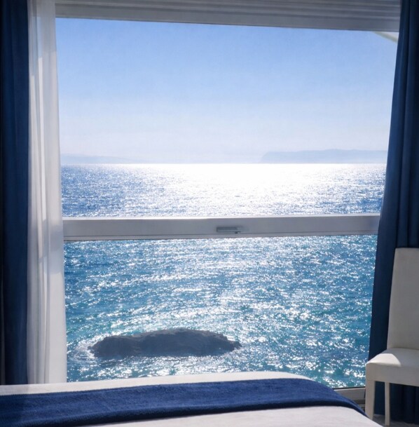 A room with a large window overlooking a body of water, a bed, and a chair.
