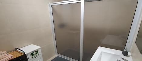 A bathroom with a shower, a sink, a mirror, and a laundry cart.