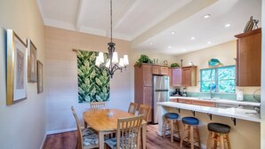 Cocina moderna con armarios de madera, un refrigerador de acero inoxidable y una zona de comedor con mesa y sillas de madera.