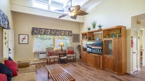 Una sala de estar con ventilador de techo, televisor y mueble de madera.