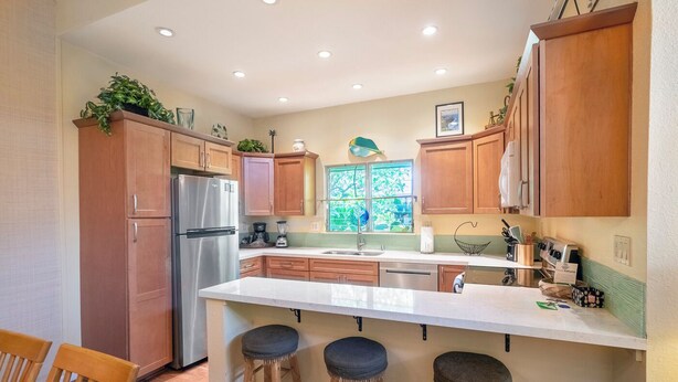 Una cocina con armarios de madera, un refrigerador de acero inoxidable, una encimera blanca y tres taburetes.