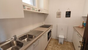 A compact kitchen with two stainless steel sinks, a window above the counter, and a small trash bin. - Attraktive Ferienwohnung am Luganer See (Porlezza)