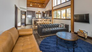 A spacious living room with a leather sofa, a round coffee table, and a blue rug. - Ski In/Out home 50 steps to Bear Back Poma Lift w/steam shower - Big Horn Escape (Big Sky)