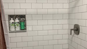 A shower area with white subway tiles, a showerhead, and a shelf with toiletries. - Home Sweet Home, minutes to Great Lakes Naval Base (Lake Bluff)