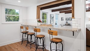 Een keuken met een witte inrichting, houten barstoelen en een groot raam.