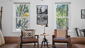 Een kamer met twee leren fauteuils, een tafeltje met een lamp, en ingelijste foto’s aan de muur.